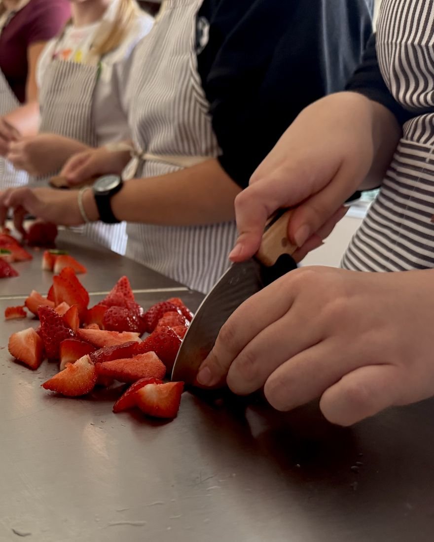 Young cooks in striped aprons chopping strawberries at a Cooking for Kindness session